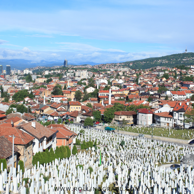 A peaceful Sarajevo cemetery with densely clustered white graves rising against a soft green slope.