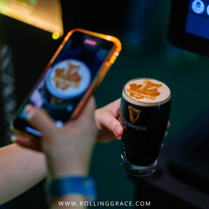 Hand holding a phone photographing a Guinness Draught pint at a St. Patrick's event in Malaysia