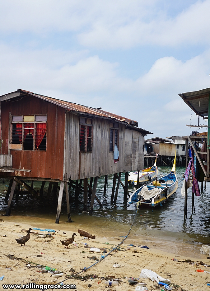 Sandy beach at Kampung Mabul with stilt houses and a boat in the background, Pulau Mabul, Sabah
