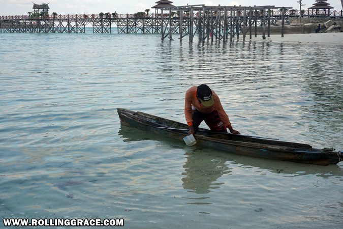 Bajau Laut fisherman rowing a wooden boat on calm sea at Pulau Mabul Sabah Malaysia