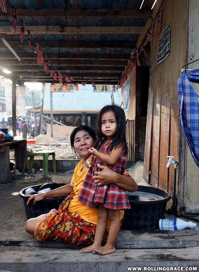 Bajau Laut girl sitting on wooden floor beside cooking pot at Pulau Mabul Sabah