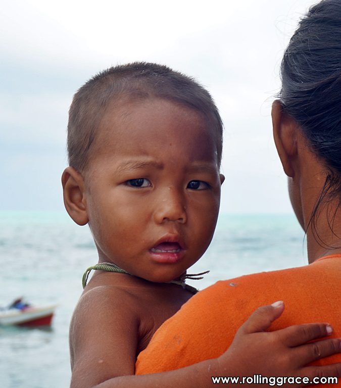 Bajau Laut mother holding toddler on a wooden boat on turquoise sea Sabah Malaysia