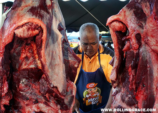 A butcher standing beside hanging raw meat at the wet market section of Nat Pokok Getah in Perlis
