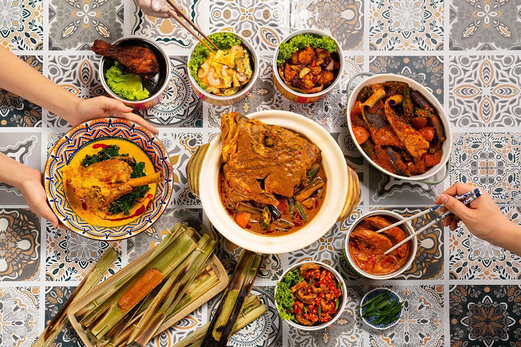 An assortment of Malaysian stir-fry dishes and curries on a patterned tile table at Chan Mari Chan Muhibah Bistro