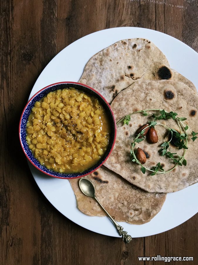 Homemade chapati served on a white plate with a bowl of dal on a dark wooden table