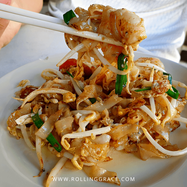 Plate of char kuey teow with flat rice noodles, prawns, cockles, bean sprouts, and egg fried with wok hei in Penang