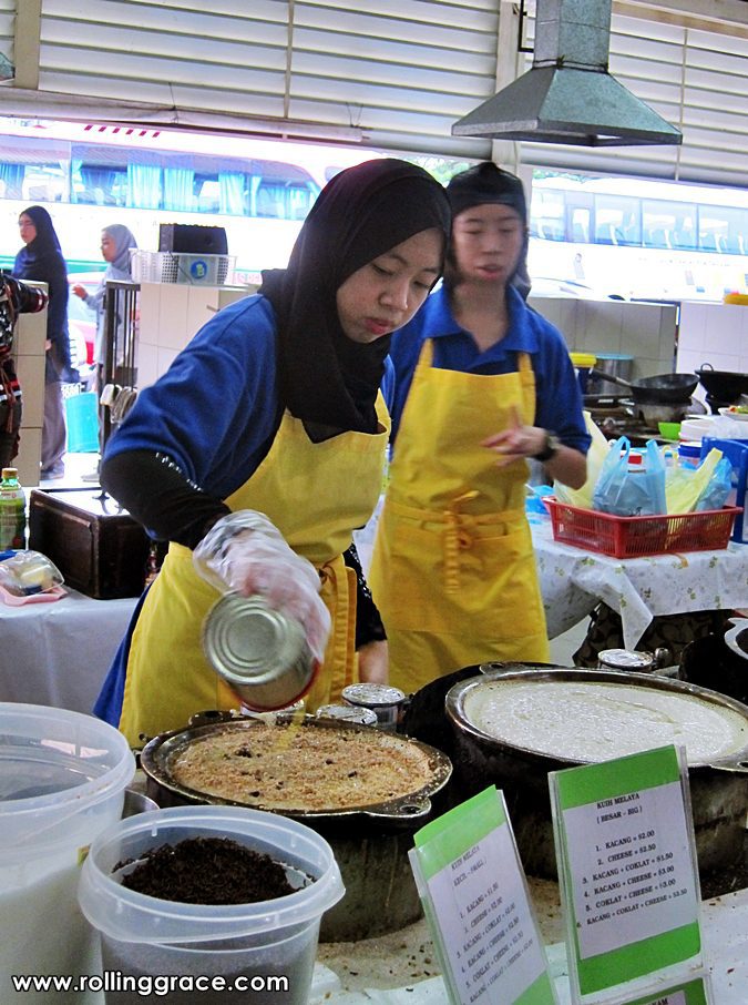 A female vendor in a yellow apron serving kuih and snacks at her stall in Gadong Night Market, Brunei