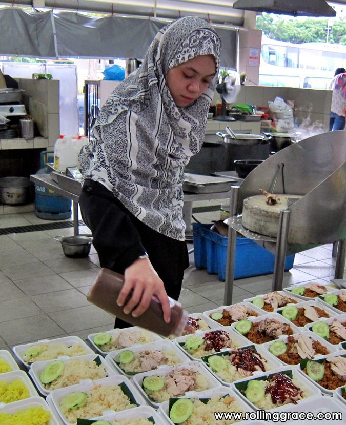 A female vendor in a headscarf arranging trays of nasi campur and cooked dishes at Gadong Night Market in Brunei