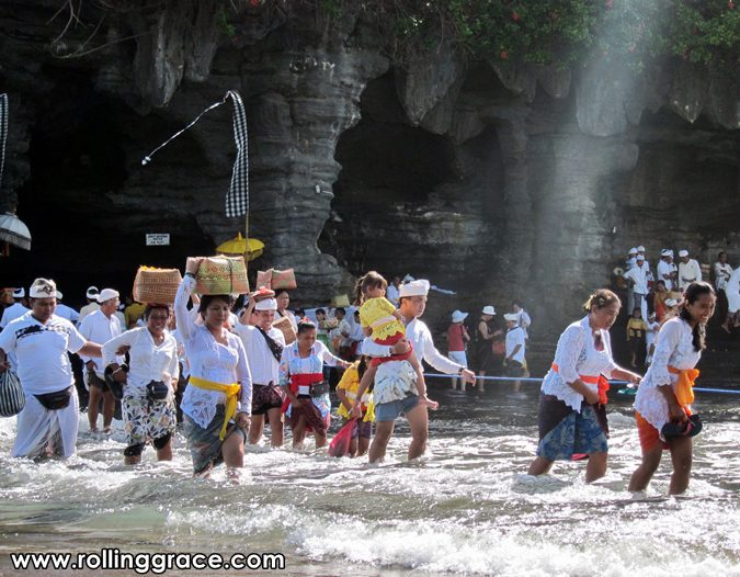 Visitors walking across the path to the base of Tanah Lot temple at low tide
