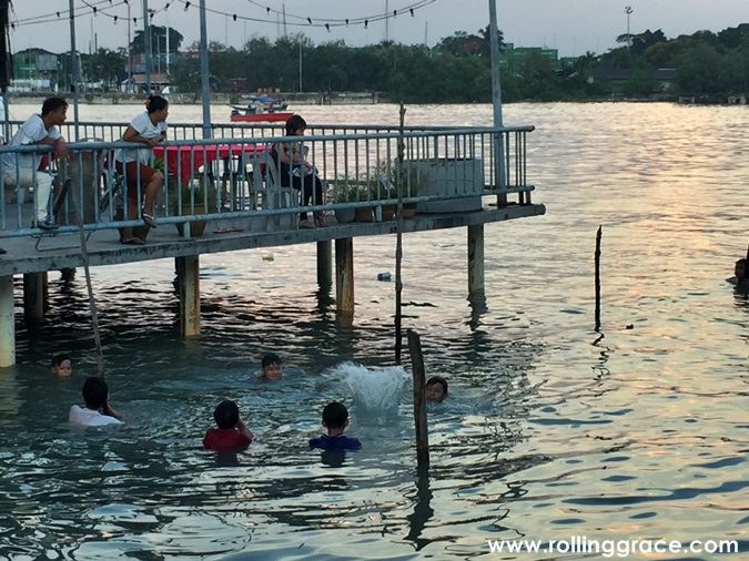 Children swimming in the Klang River off a wooden jetty at Bagan Hailam fishing village, Port Klang, at sunset.