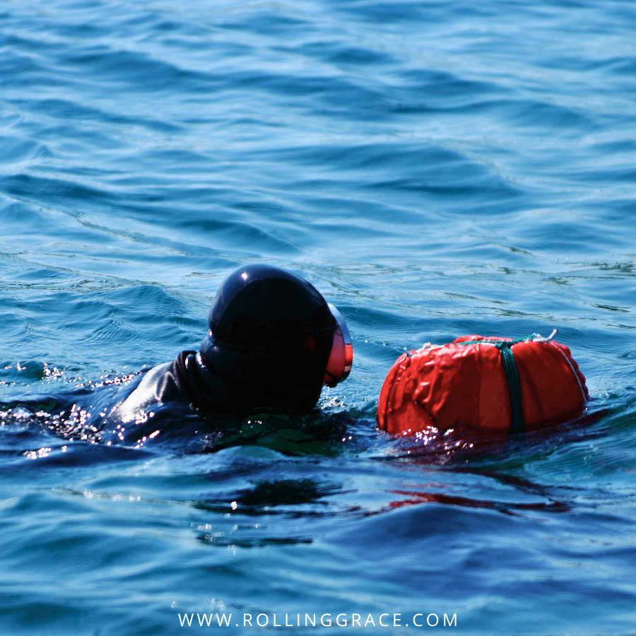 Haenyeo diver surfacing from the ocean wearing a black wetsuit with orange tewak float visible on the water, Jeju Island.