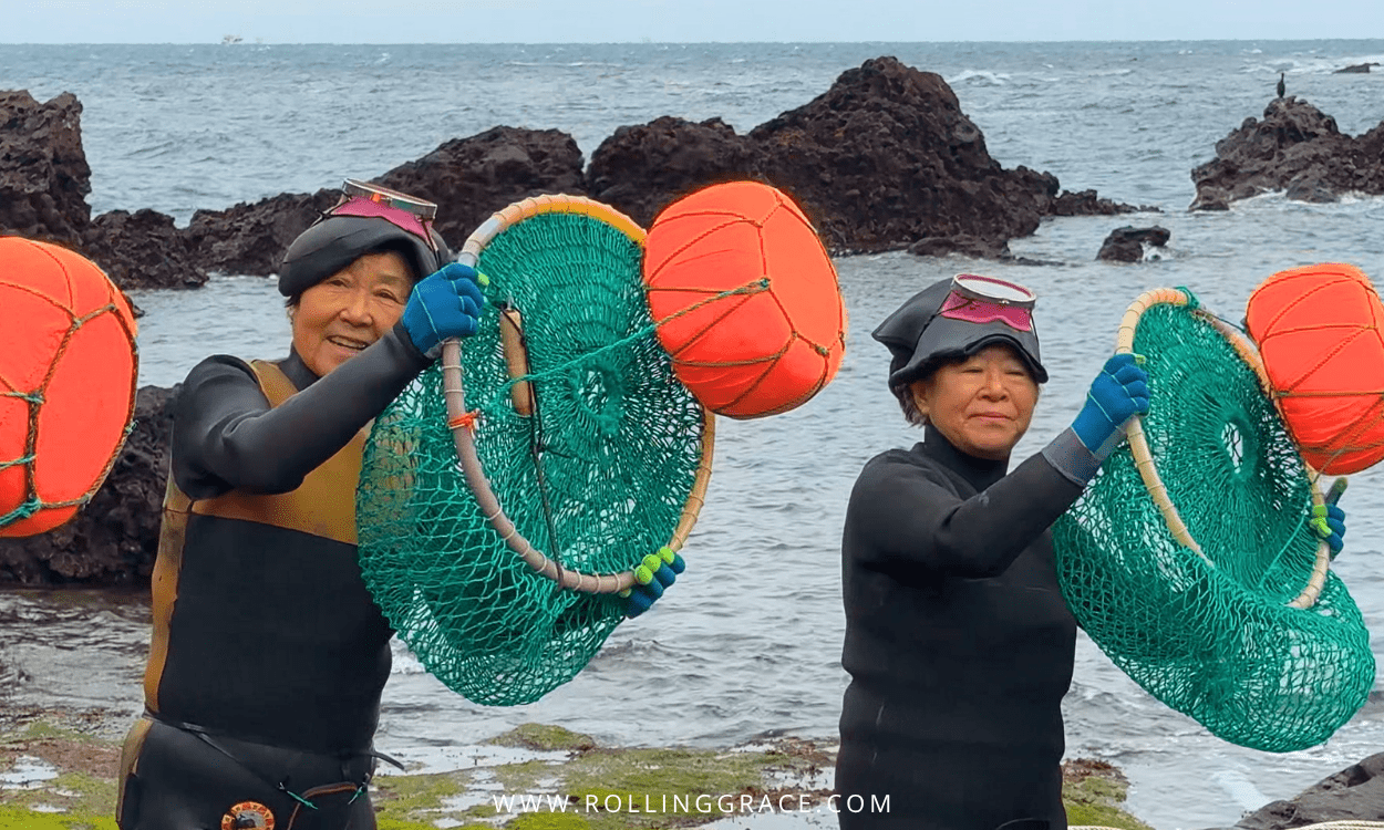 Haenyeo divers on the rocky coastline of Jeju Island carrying orange tewak floats and green harvest nets after a dive.