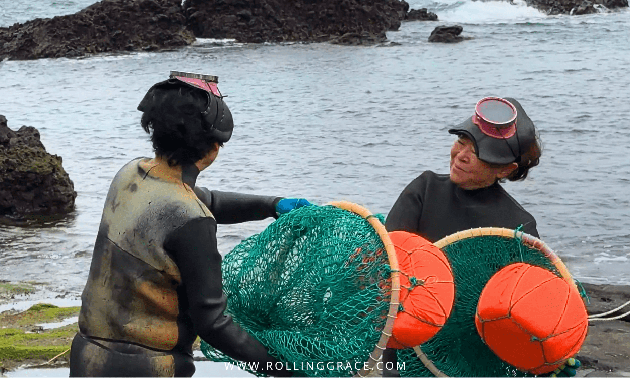 Haenyeo diver wading into the ocean from the rocky shore of Jeju Island, South Korea, carrying a tewak float.