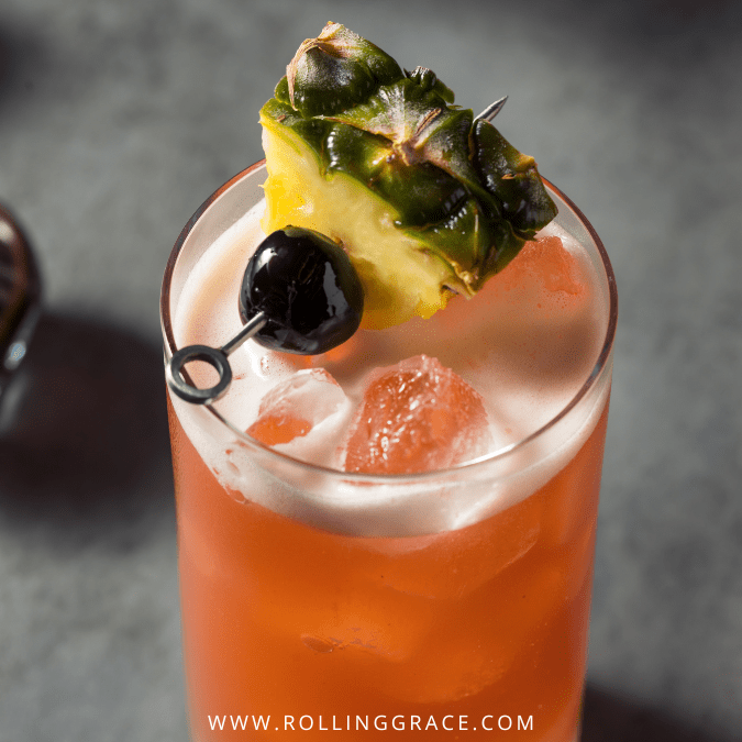 Close-up of a Singapore Sling cocktail with pineapple top and cherry garnish on ice.