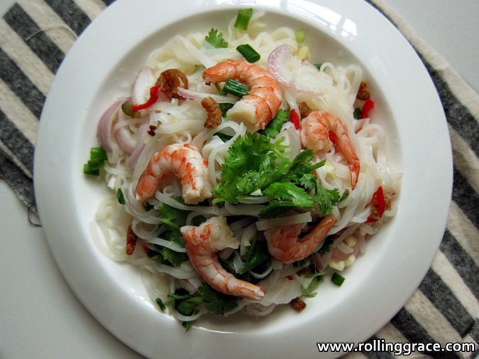 Thai spicy noodle salad recipe Yum Sen Mee with poached shrimp, red chilli, and fresh herbs on a white plate.