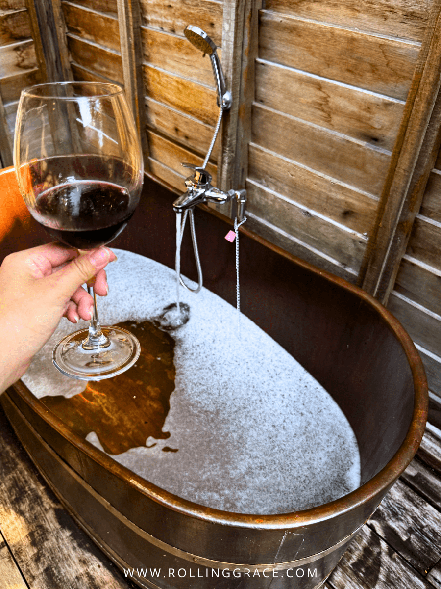 Hand holding a glass of red wine beside an outdoor bathtub at Bon Ton Resort, Langkawi, Malaysia