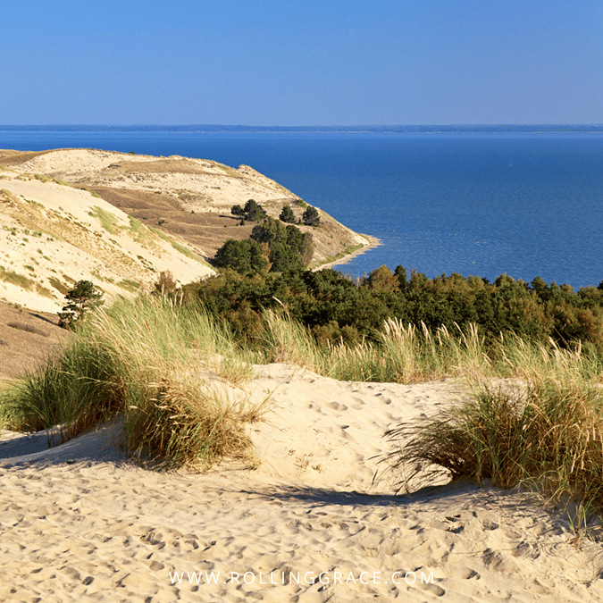 Exploring Curonian Spit Lithuania: 10 Amazing Things to Do 3 Sand dunes covered in wild grass with the Baltic Sea visible in the background on the Curonian Spit Lithuania