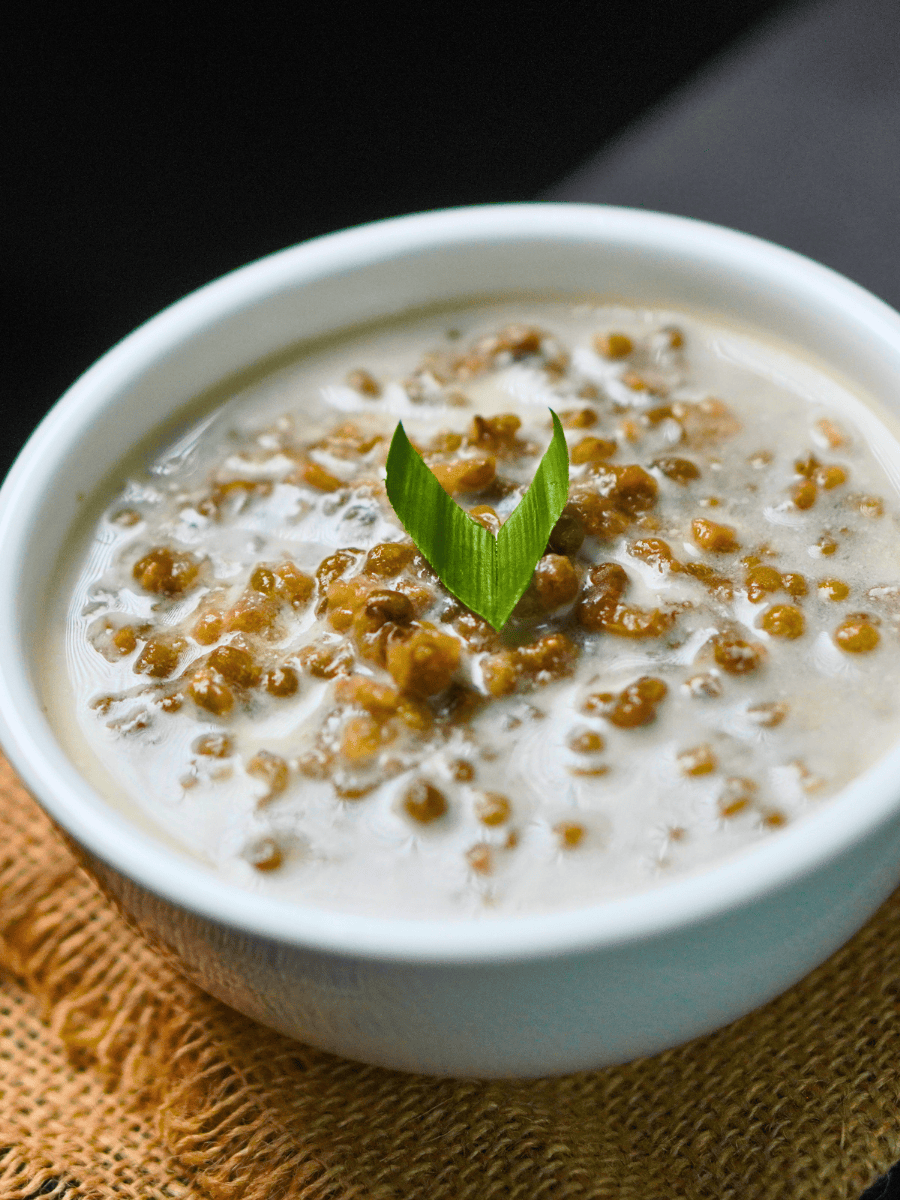 Mung bean soup recipe with coconut milk served in a white bowl with a pandan leaf garnish
