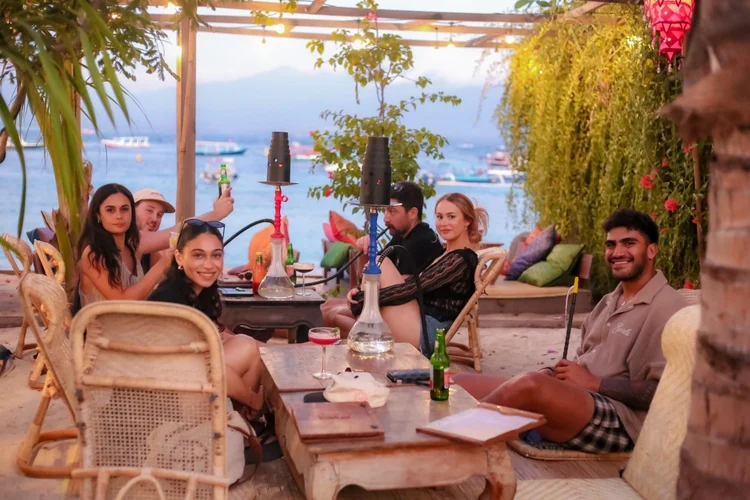 8 Best Shisha in Lombok for a Stunning Sunset Session 6 Guests relaxing with shisha on a plant-filled terrace at Pesona Lounge Gili Trawangan