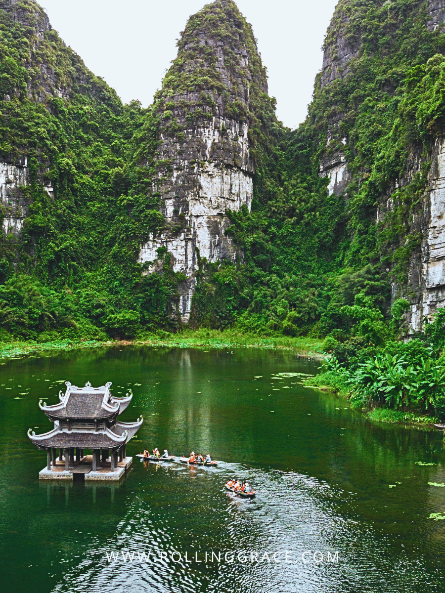 Sampan boat on emerald water with limestone karsts and pagoda at Trang An Landscape Complex Ninh Binh