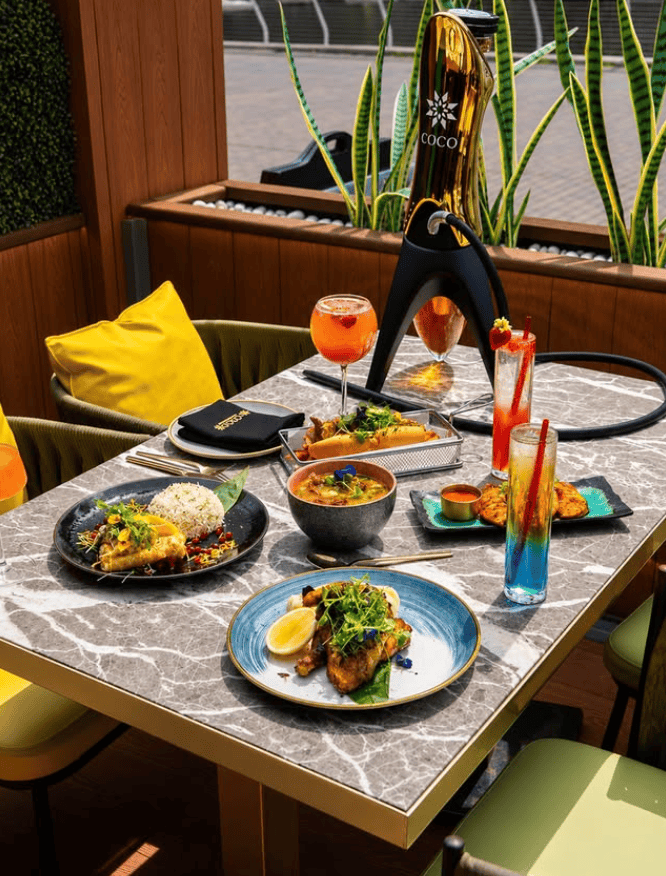 COCO Canary Wharf shisha lounge with colourful cocktails and grilled dishes at a dockside table
