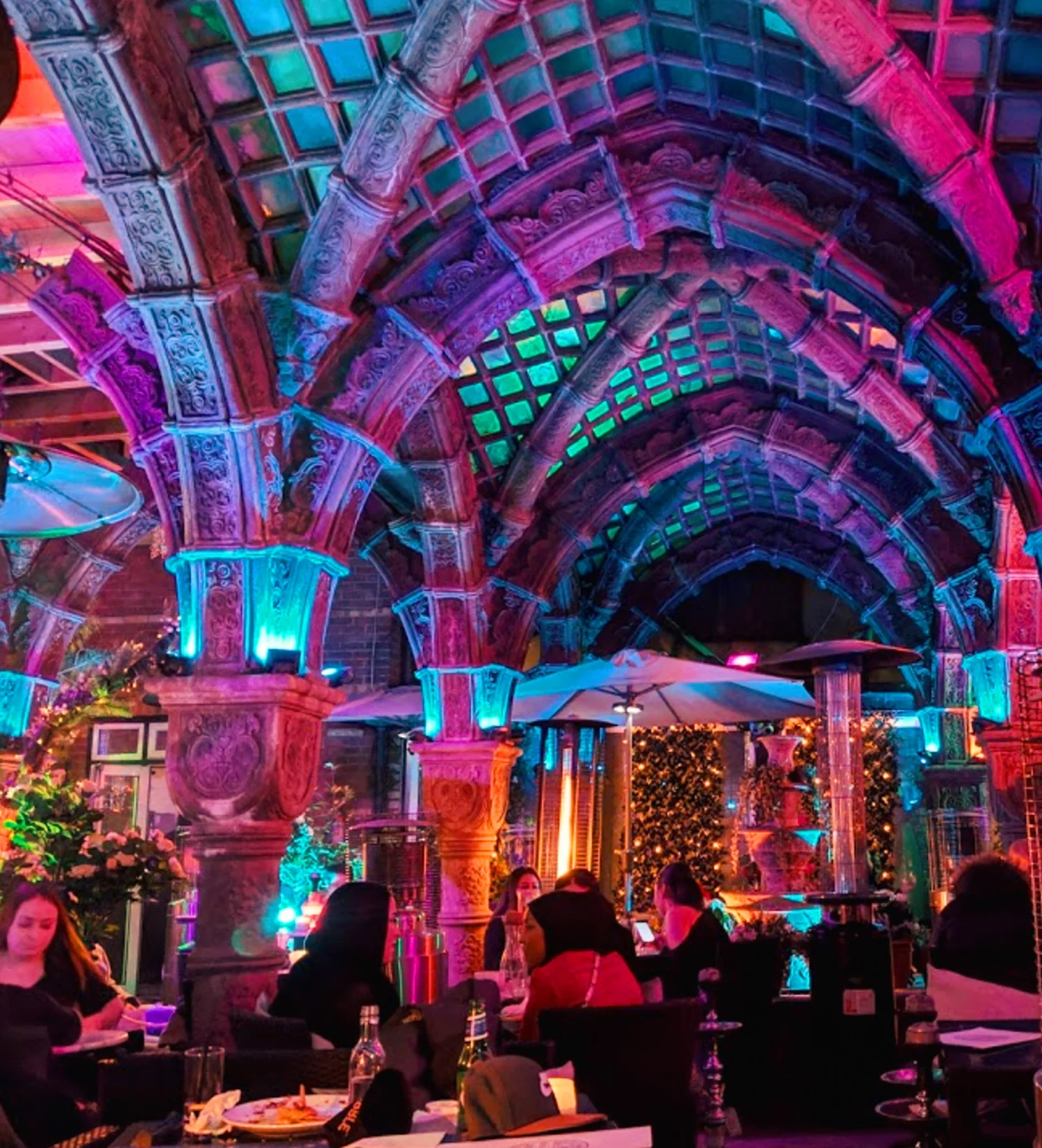 The Shisha Garden Edgware with colourful ambient lighting and hookah setup in a lush courtyard setting