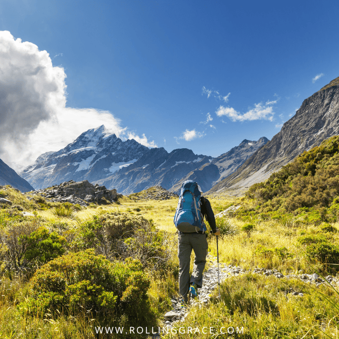 Solo hiker on a trail overlooking mountains and coastline in New Zealand one of the safest countries for solo female travel