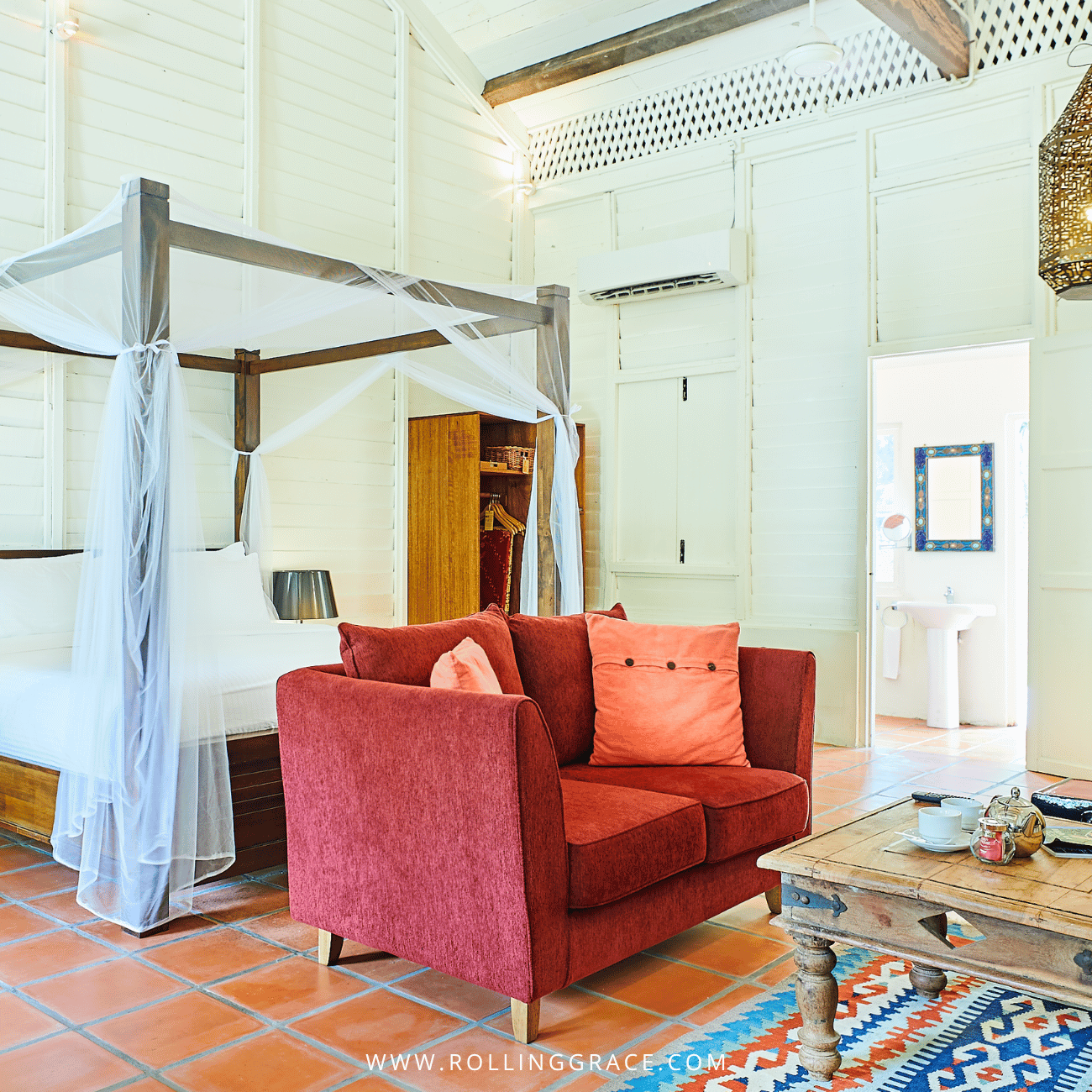Canopy bed, red armchair and terracotta floor in an Estate House bedroom at Temple Tree Resort Langkawi