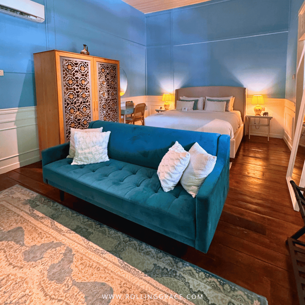 Sky-blue Straits House bedroom with a teal sofa and carved wardrobe at Temple Tree Resort Langkawi