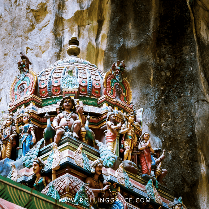 Ornate temple tower covered in painted Hindu figures against the limestone cliff face at Batu Caves