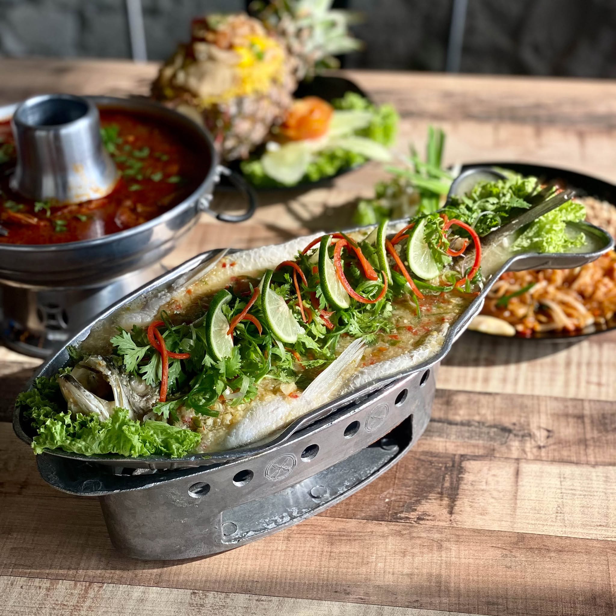 Whole steamed fish with lime and herbs in a fish-shaped tray beside a tom yum pot at Soi 55 Thai Kitchen, Bukit Tinggi Klang