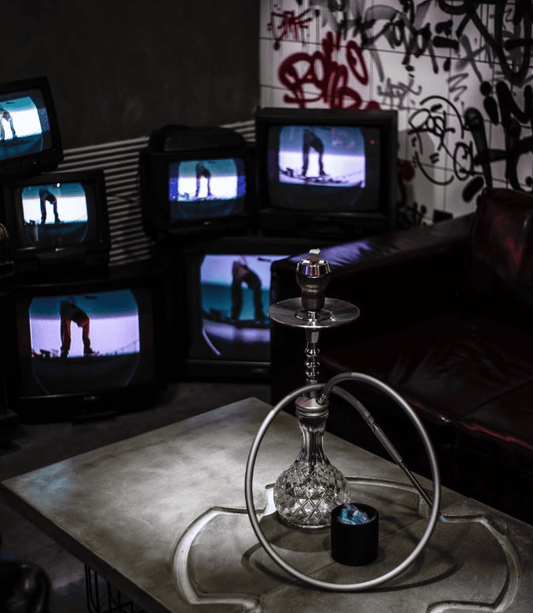 Hookah on a table in front of stacked retro TV screens and a graffiti wall at HookahPlace Forever, shisha in Moscow