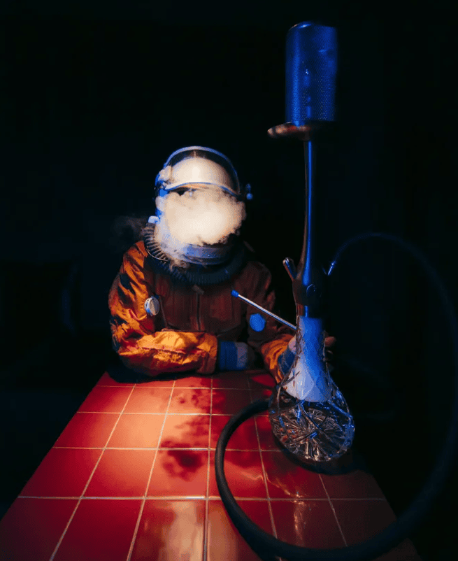 Figure in an orange space suit and helmet exhaling smoke beside a blue glass hookah at HookahPlace Futura, shisha in Moscow